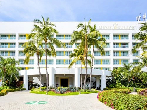 White resort exterior and covered entrance surrounded by tropical palm trees and landscaped greenery.