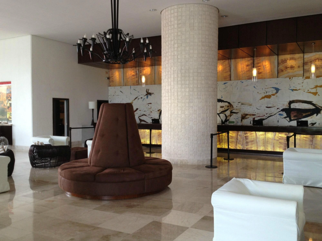 Spacious Mayan Palace lobby featuring round brown seating, polished marble floors, and a modern chandelier.
