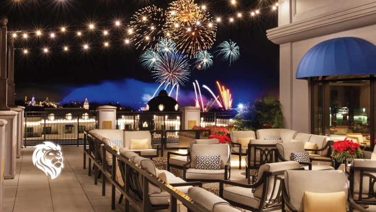 Rooftop terrace with lounge seating and string lights overlooking a colorful fireworks display at night.
