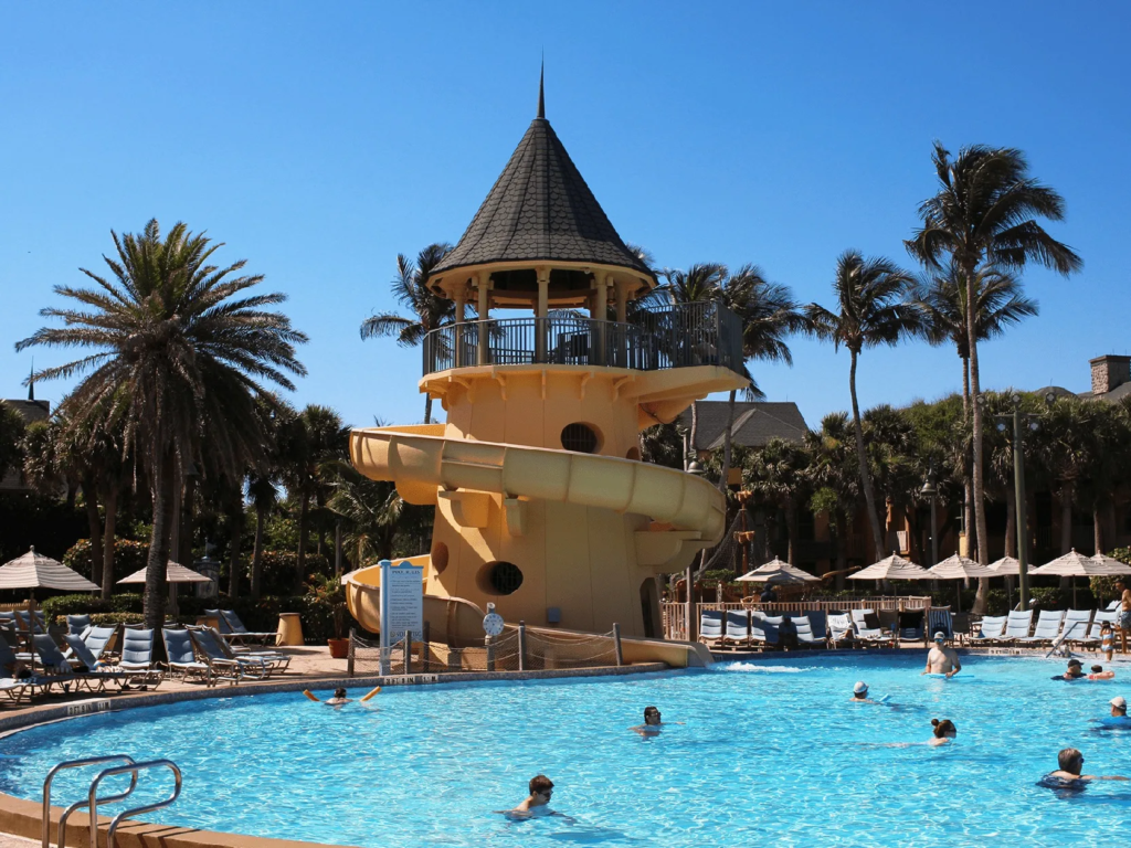 Resort pool with a yellow spiral water slide and palm trees at Disney's Vero Beach Resort.