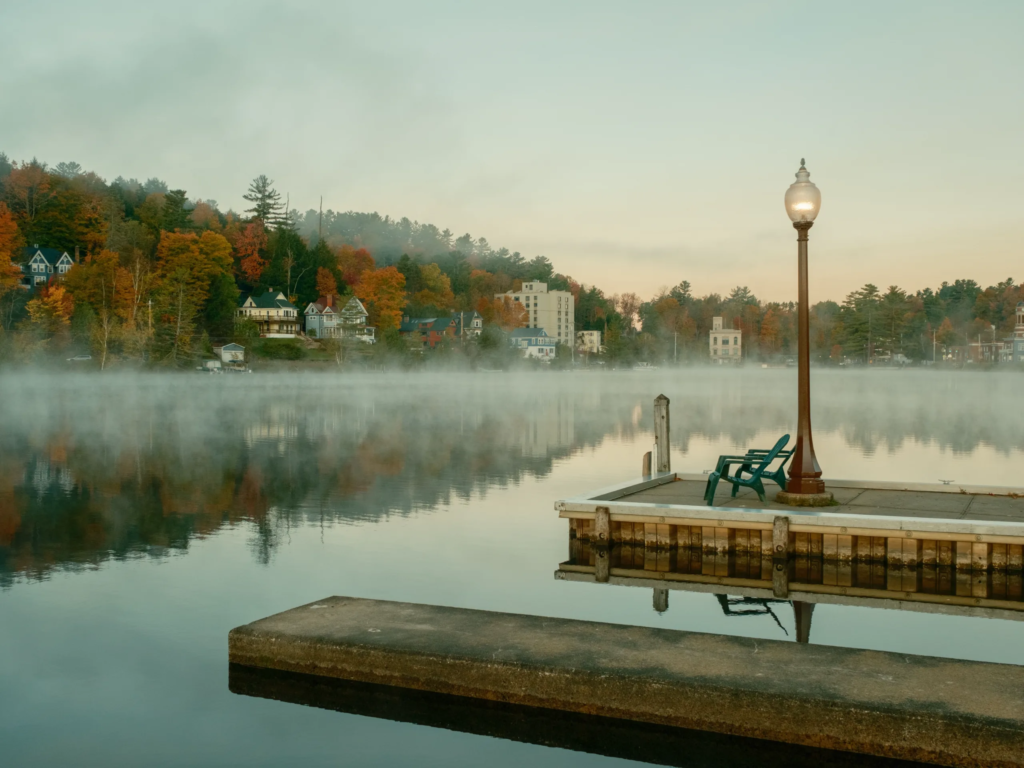 Misty autumn dock on a calm Adirondack lake—perfect for romantic getaways in upstate NY with scenic chairs and lakeside town views.