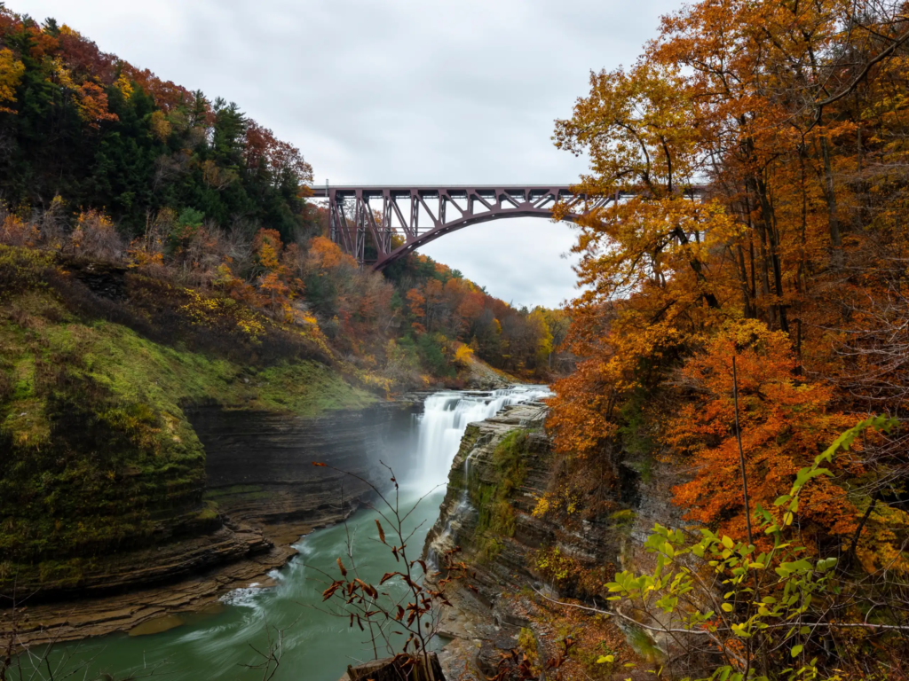 Steel arch bridge over a rocky gorge, ideal for romantic getaways in upstate NY, with autumn waterfall views.