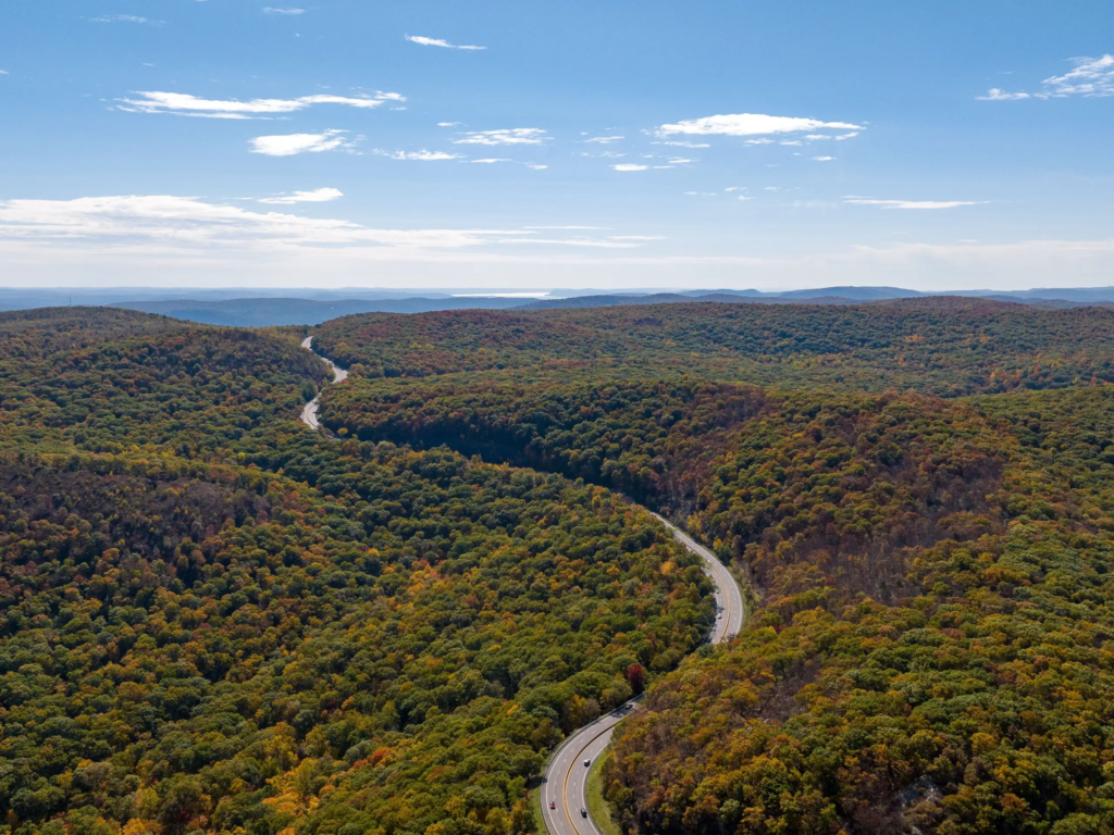Aerial view of a winding highway cutting through dense autumn forest in the Hudson Valley hills