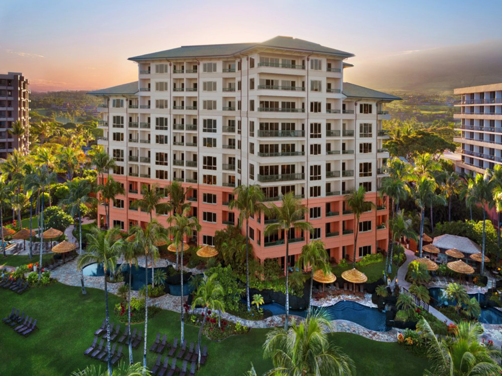 Exterior of Marriott's Maui Ocean Club featuring swimming pools, lush palm trees, and lit rooms at sunset.