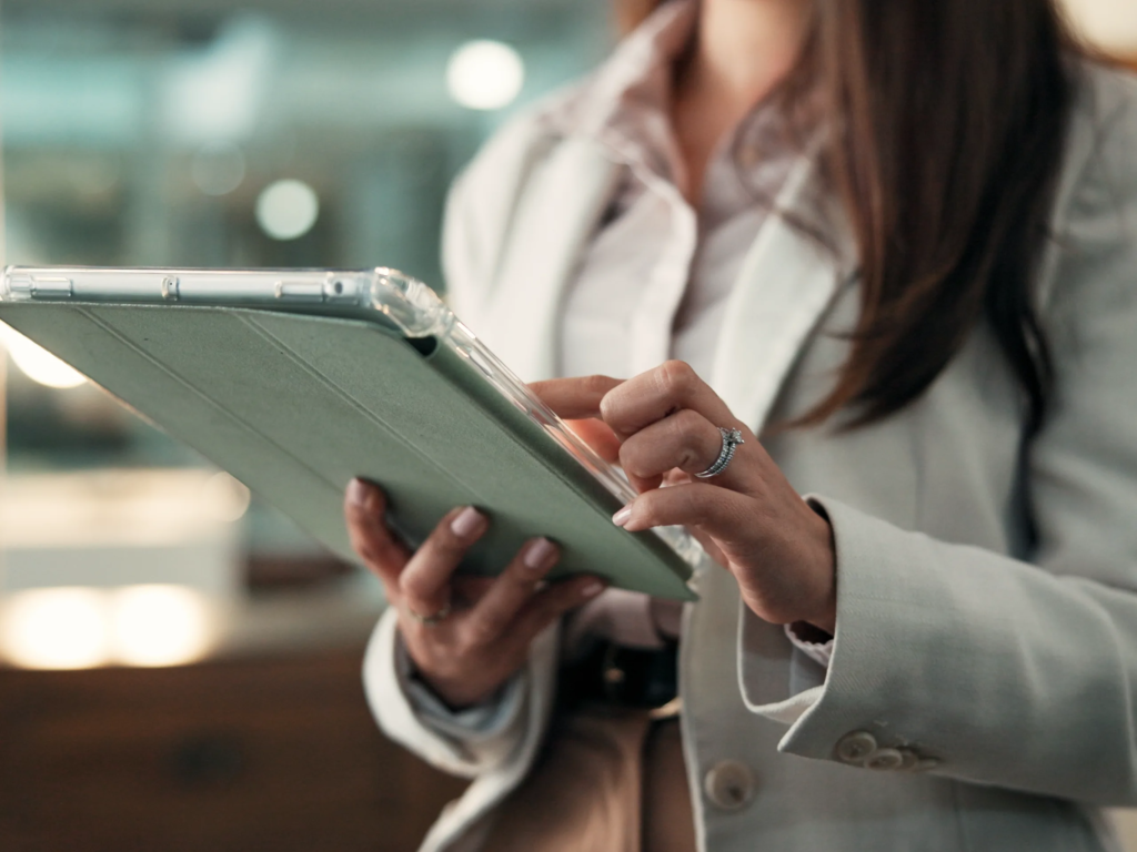 Woman in a white blazer using a tablet with a sage green protective case in a modern indoor setting.