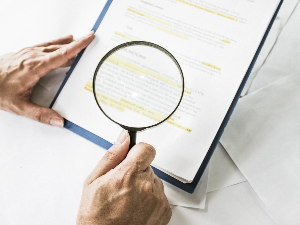 Person researching how to cancel my timeshares Boca Raton contract, using a magnifying glass on highlighted folder documents.