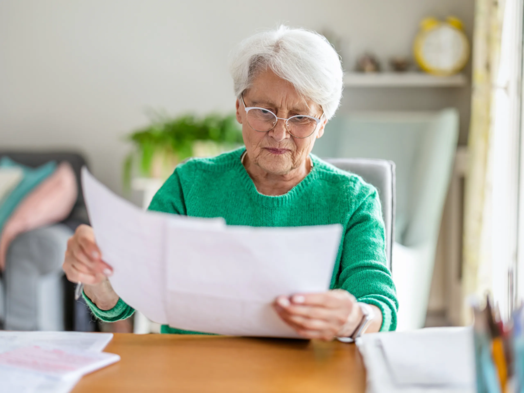 Older woman learning how to cancel my timeshares boca raton reviews documents at a sunlit wooden desk.